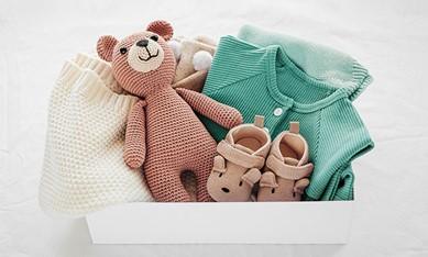 Image of a baby shower present including a teddy bear, booties, a onesie, and blanket