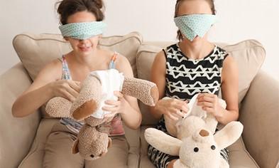 Image of two people blindfolded playing a baby shower game by trying to put a diaper on a teddy bear.